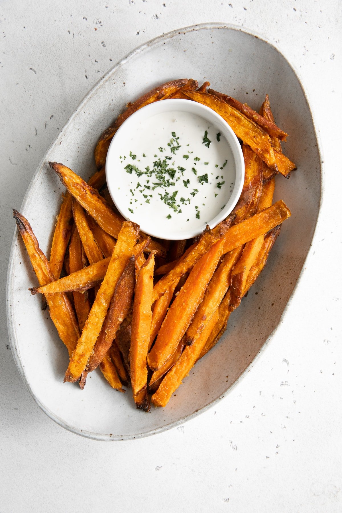 Oval serving dish filled with homemade baked sweet potato fries and served with ranch dressing.