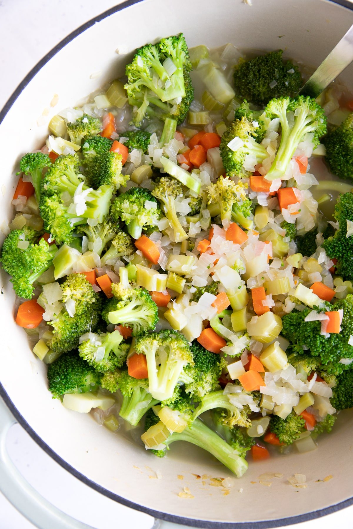 Large pot filled with softened broccoli florets, carrots, onions, and celery.