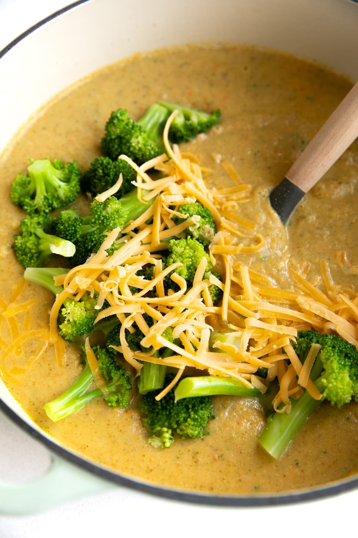 Large pot filled with cooked broccoli cheddar soup and topped with shredded cheddar cheese and blanched broccoli florets.
