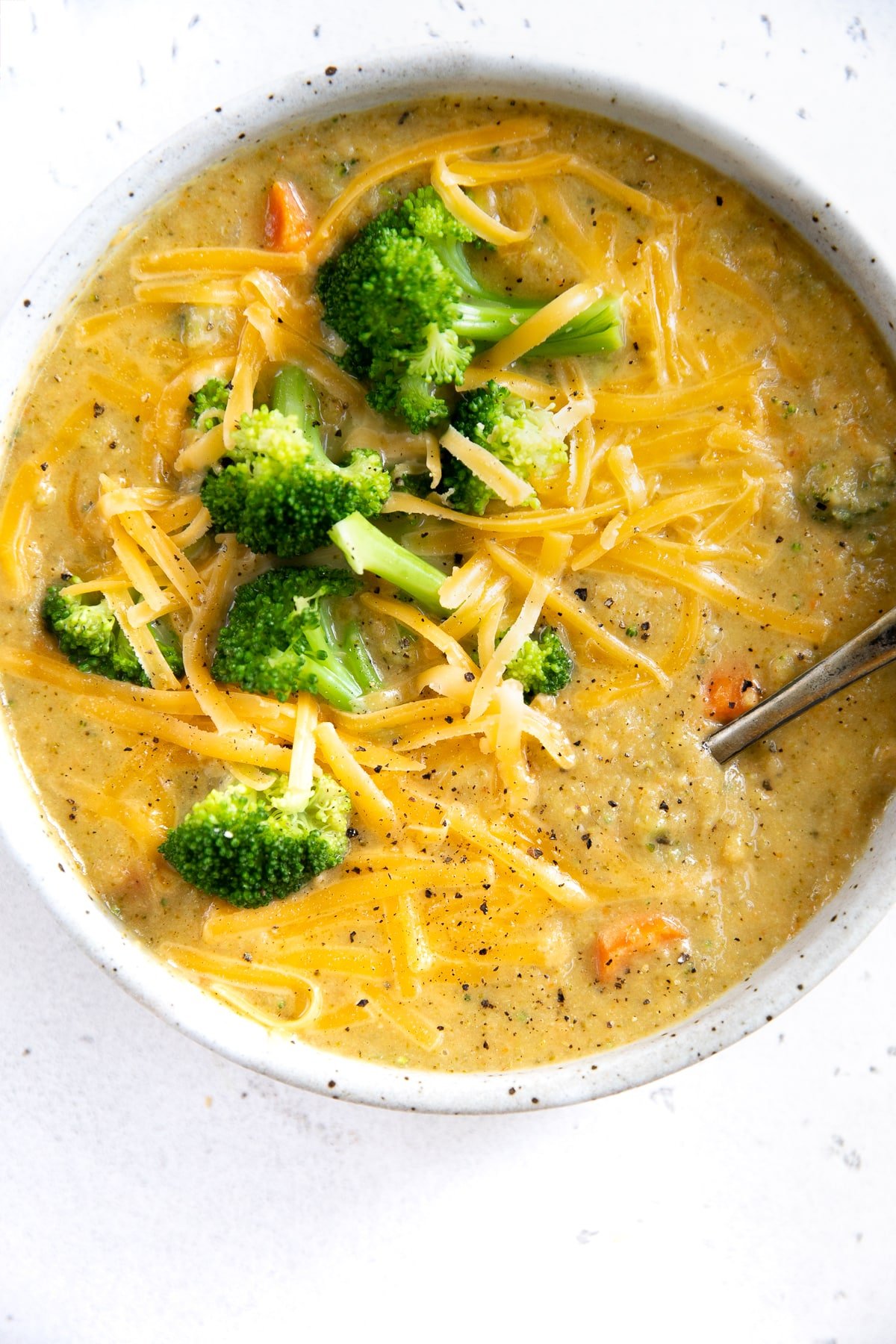 White shallow bowl filled with broccoli cheddar soup topped with blanched broccoli florets.