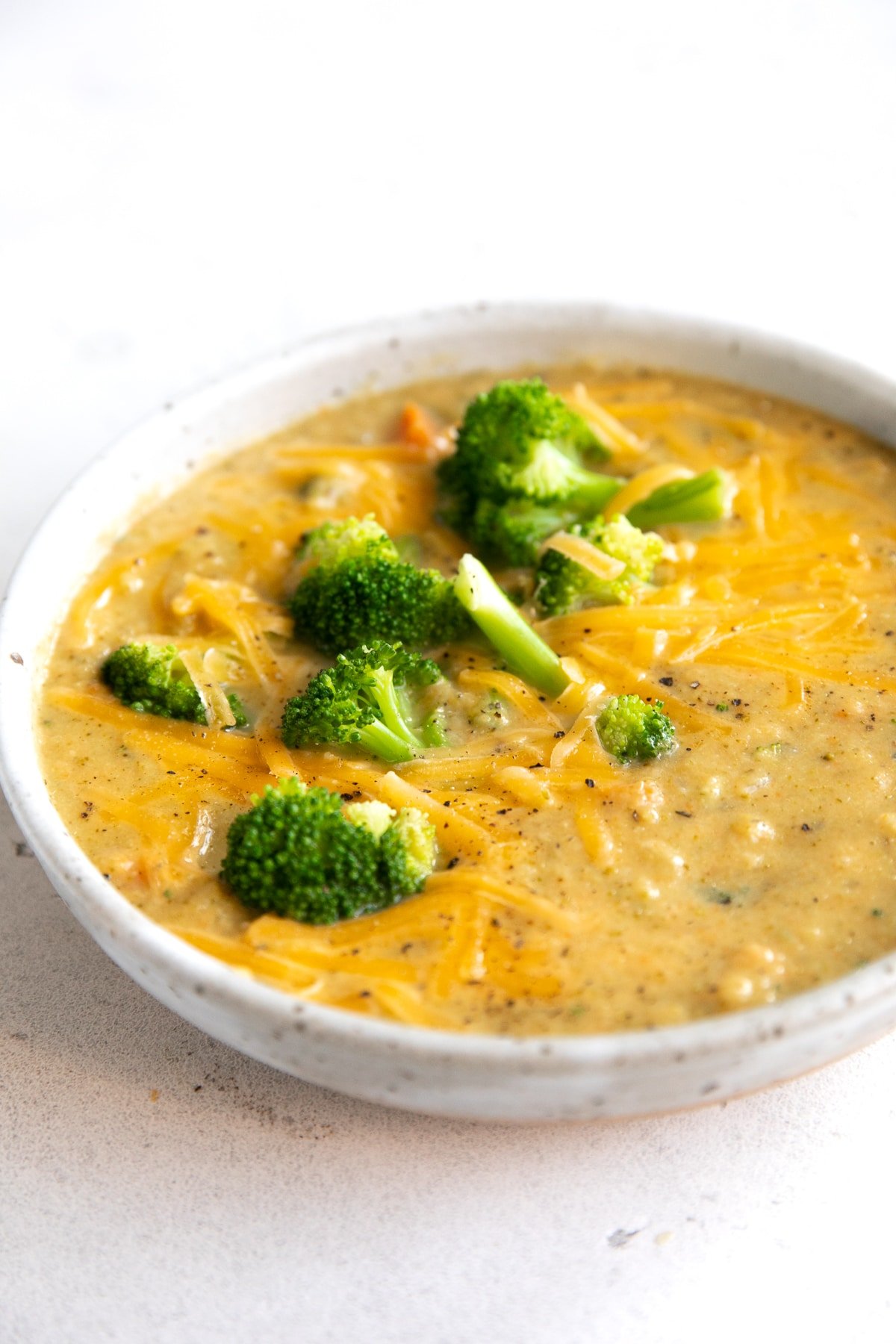 White shallow bowl filled with broccoli cheddar soup topped with blanched broccoli florets.