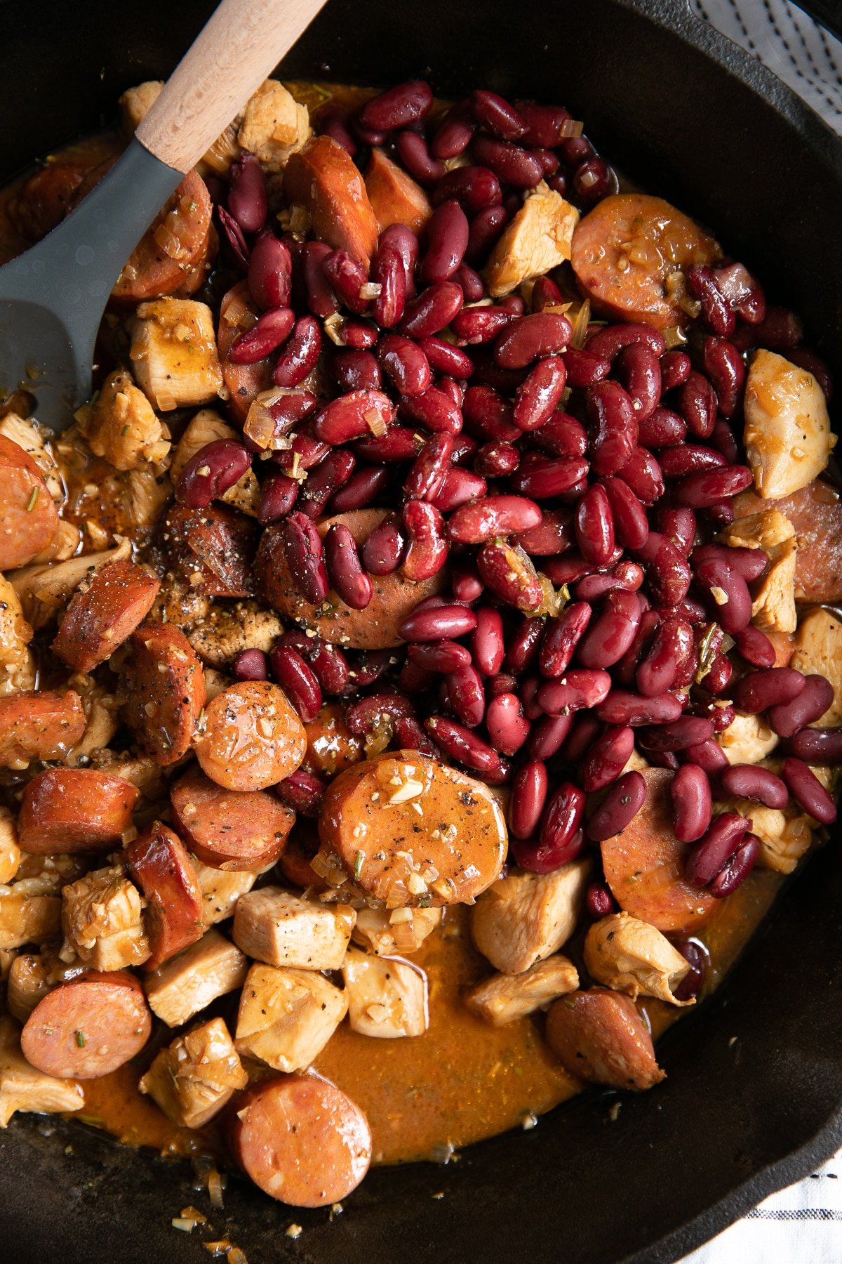 Large cast iron skillet filled with spicy cajun sausage, chicken, and kidney beans in a cajun sauce.