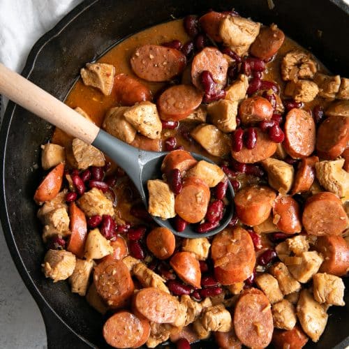 Large cast iron skillet filled with cooked andouille sausage, chicken, and kidney beans in a spicy cajun sauce.