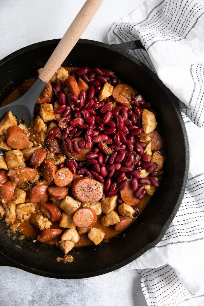 Large cast iron skillet filled with cooked andouille sausage, chicken, and kidney beans in a spicy cajun sauce.