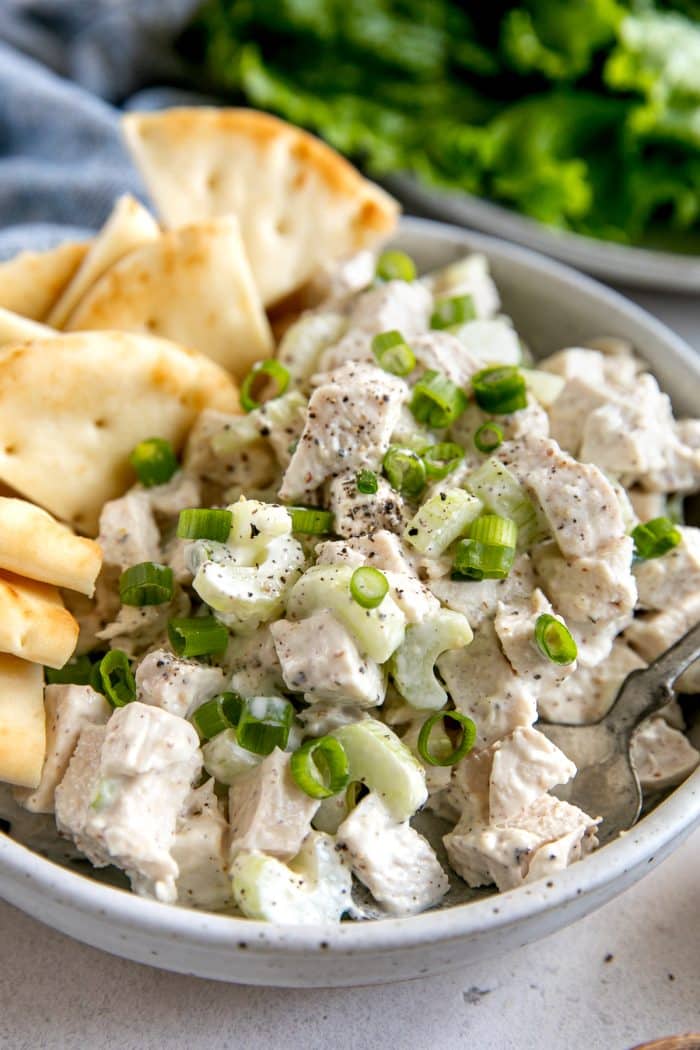 Prepared chicken salad recipe garnished with chopped green onions and served in a white serving bowl.