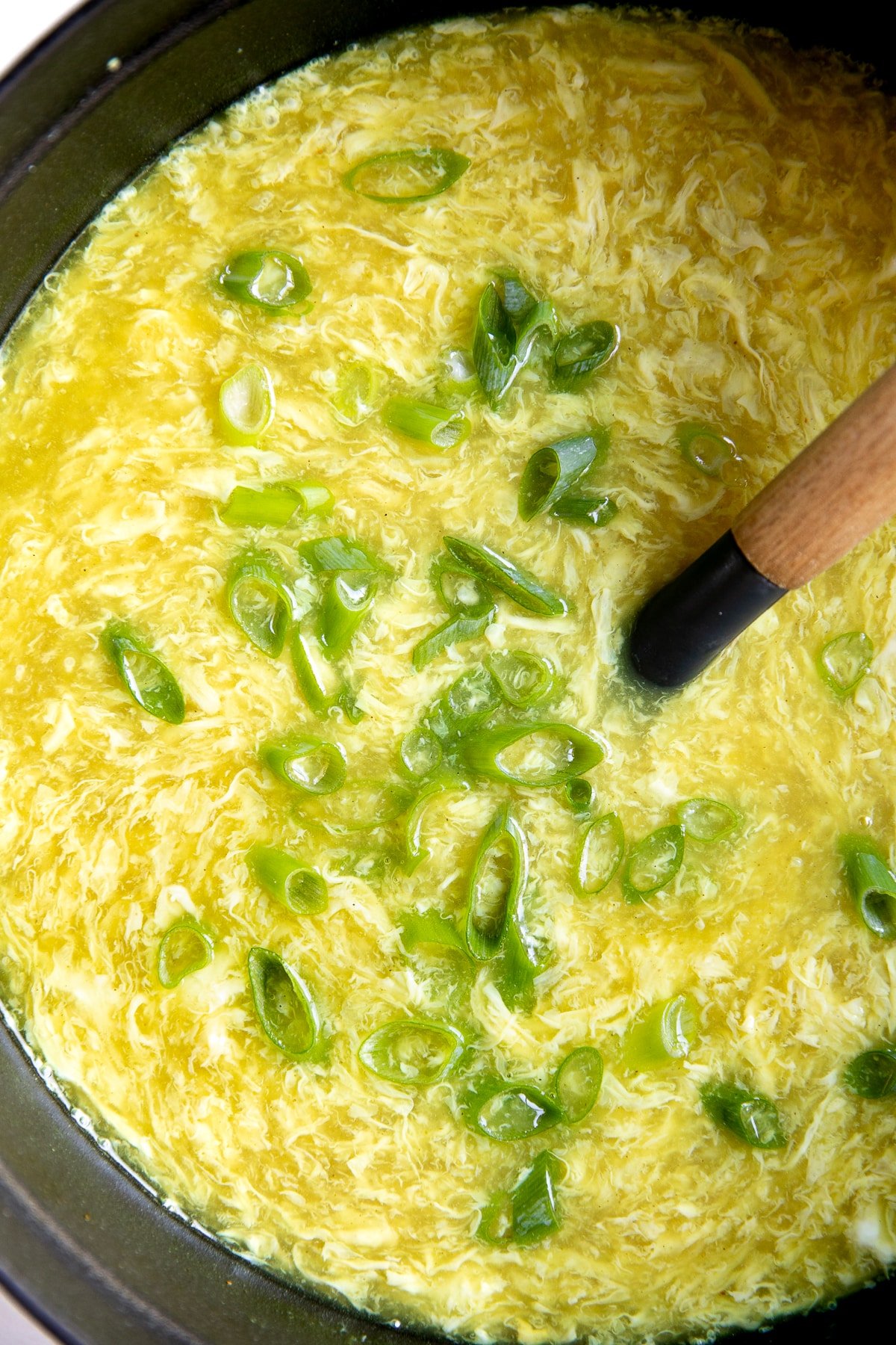 Close up image of a large pot filled with egg drop soup topped with thinly sliced green onions