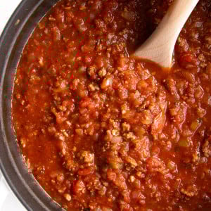 Overhead image of a large white pot filled with homemade spaghetti sauce made with onions, ground beef, garlic, and tomatoes.