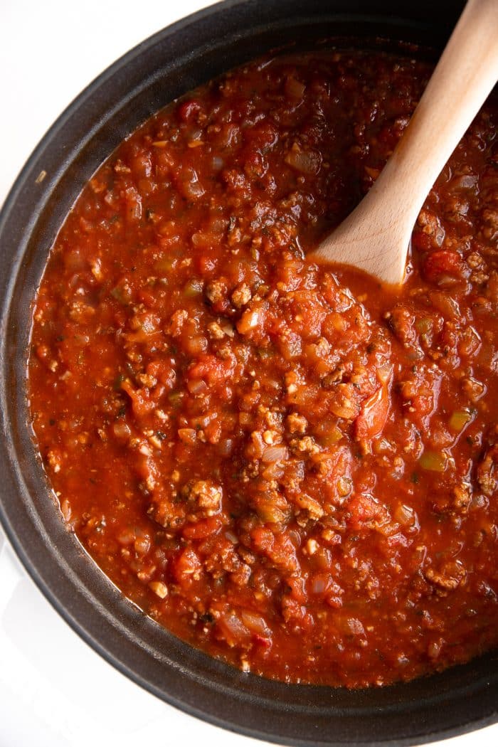 Overhead image of a large white pot filled with homemade spaghetti sauce made with onions, ground beef, garlic, and tomatoes.