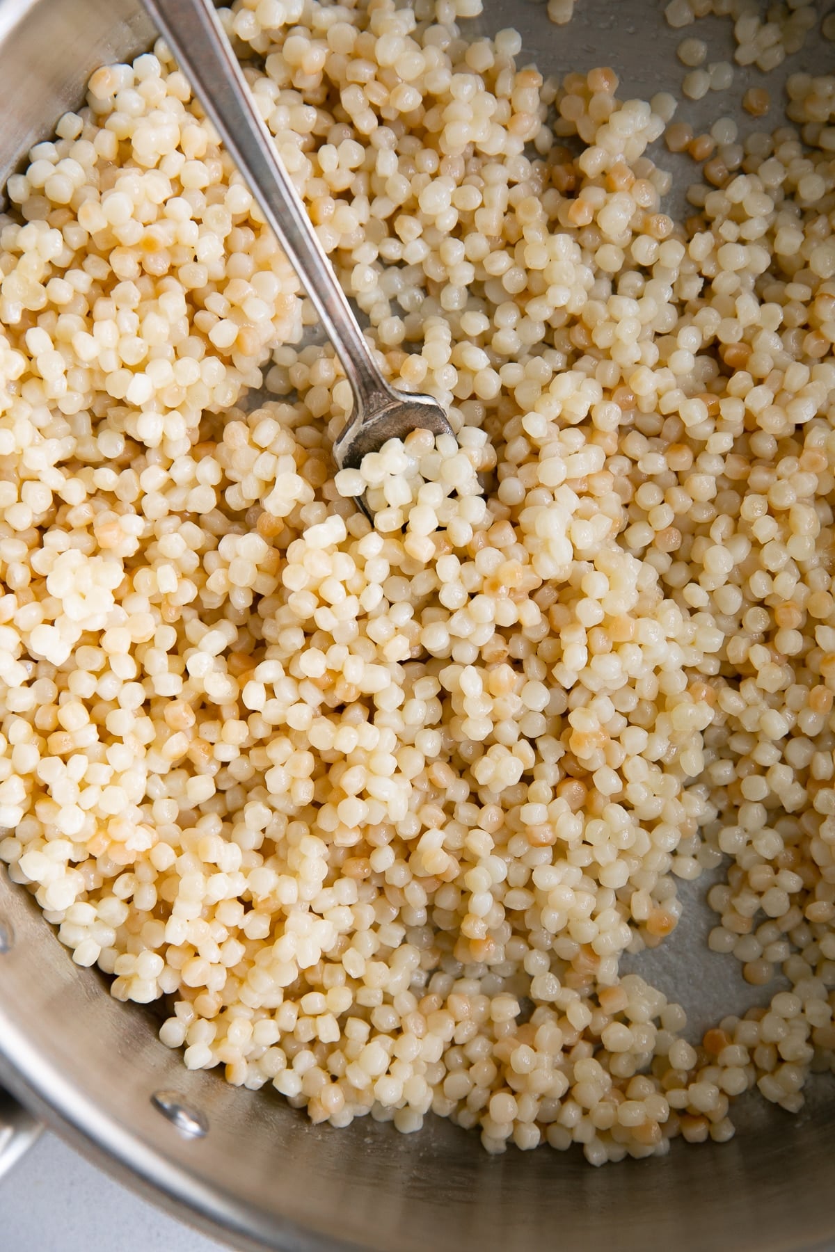 Wide saucepan filled with pearls of cooked Israel couscous.