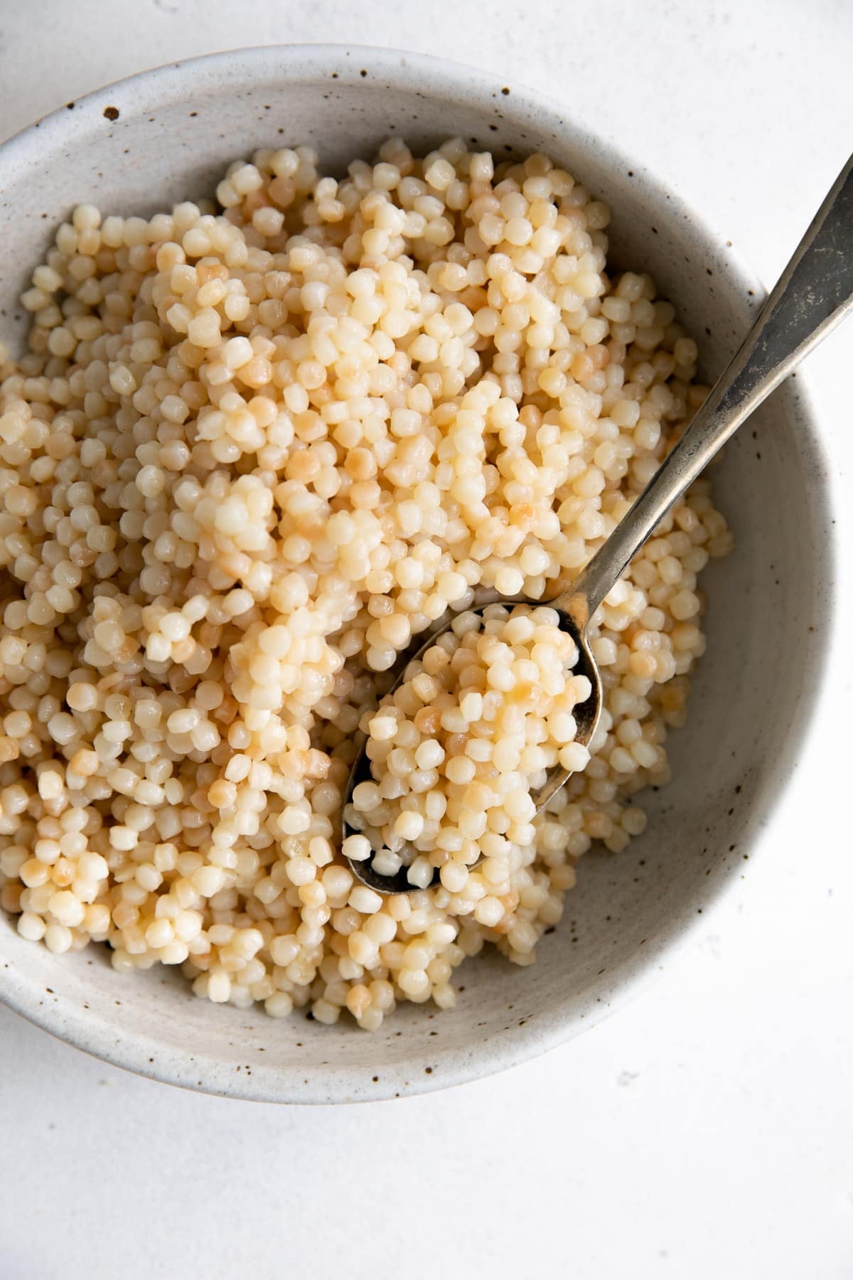 Overhead image of a large shallow bowl filled with cooked Israeli (pearl) couscous.