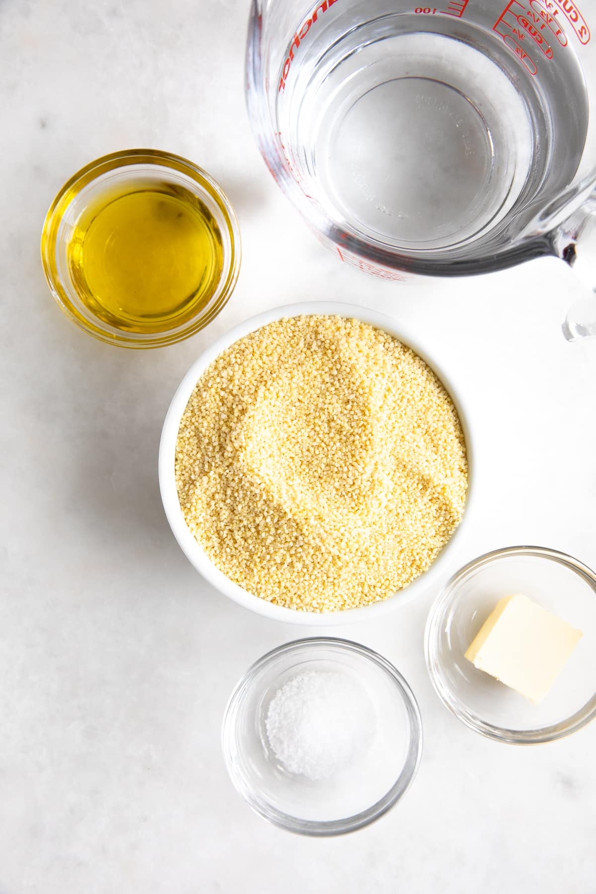 Individual bowls filled with olive oi, butter, salt, Moroccan couscous, and water.
