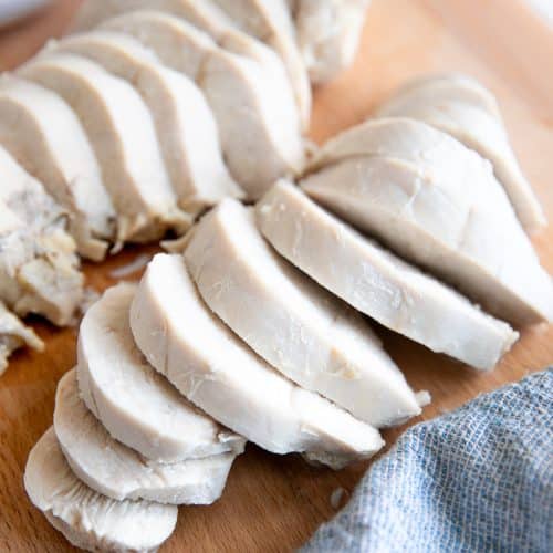 Two sliced poached chicken breasts on a wood cutting board.