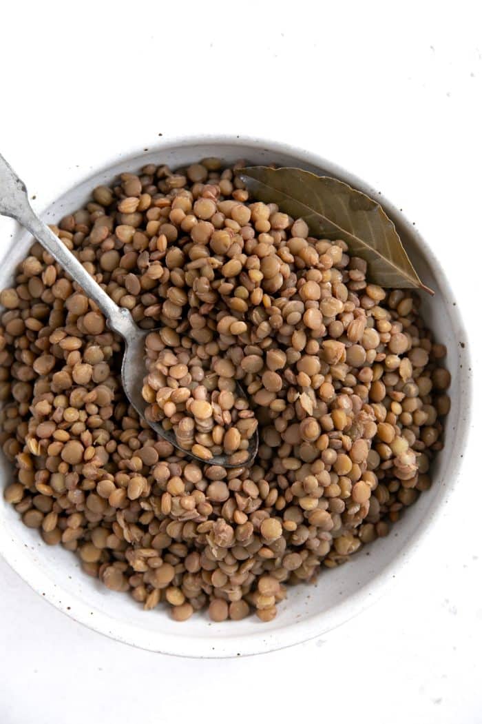Overhead image of a large white shallow bowl filled with cooked green lentils.