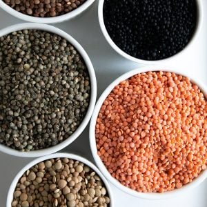 Five bowls filled with different varieties of lentils including green, brown, red, puy, and beluga.