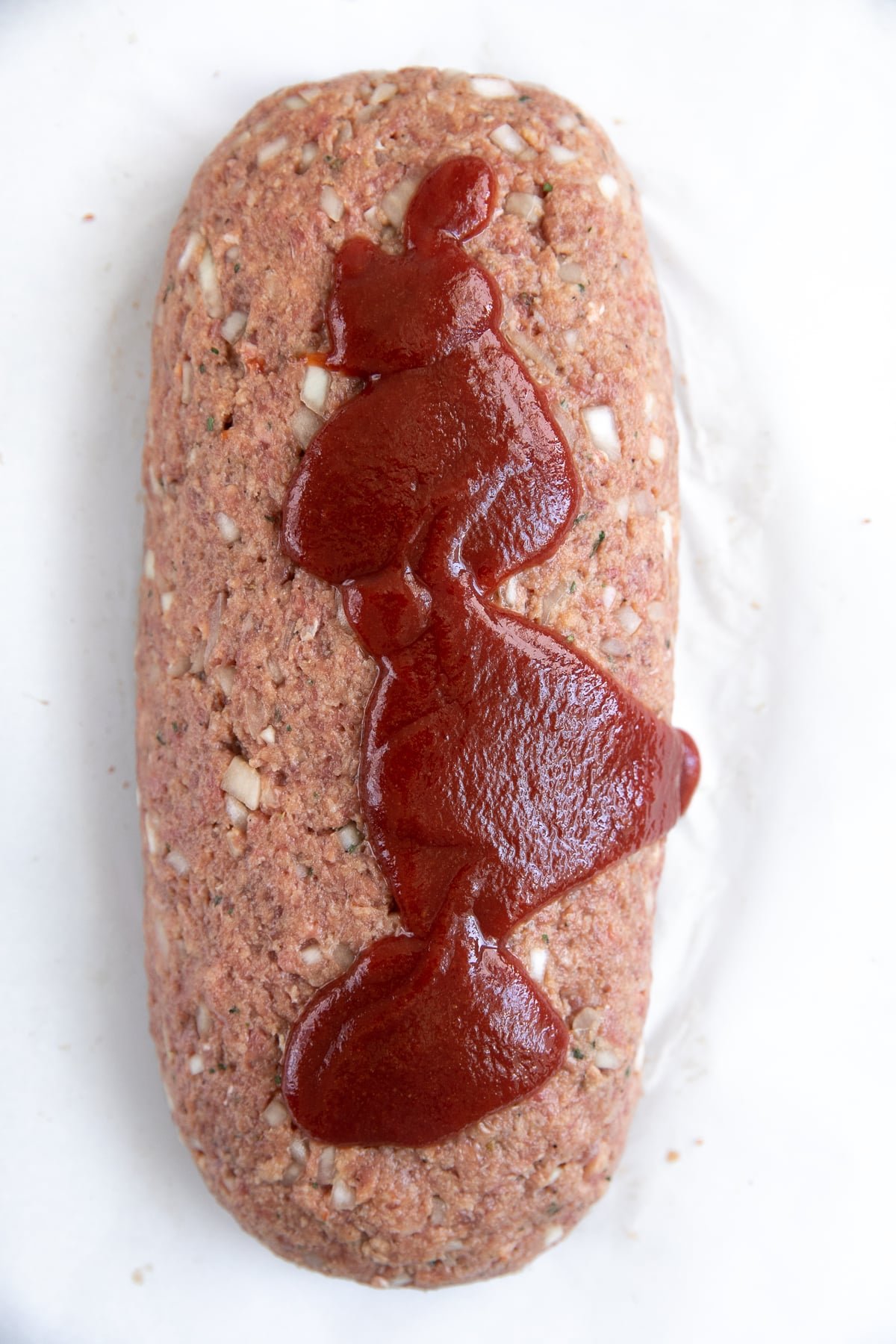 Unbaked beef meatloaf on a large parchment paper lined baking sheet topped with homemade ketchup sauce.