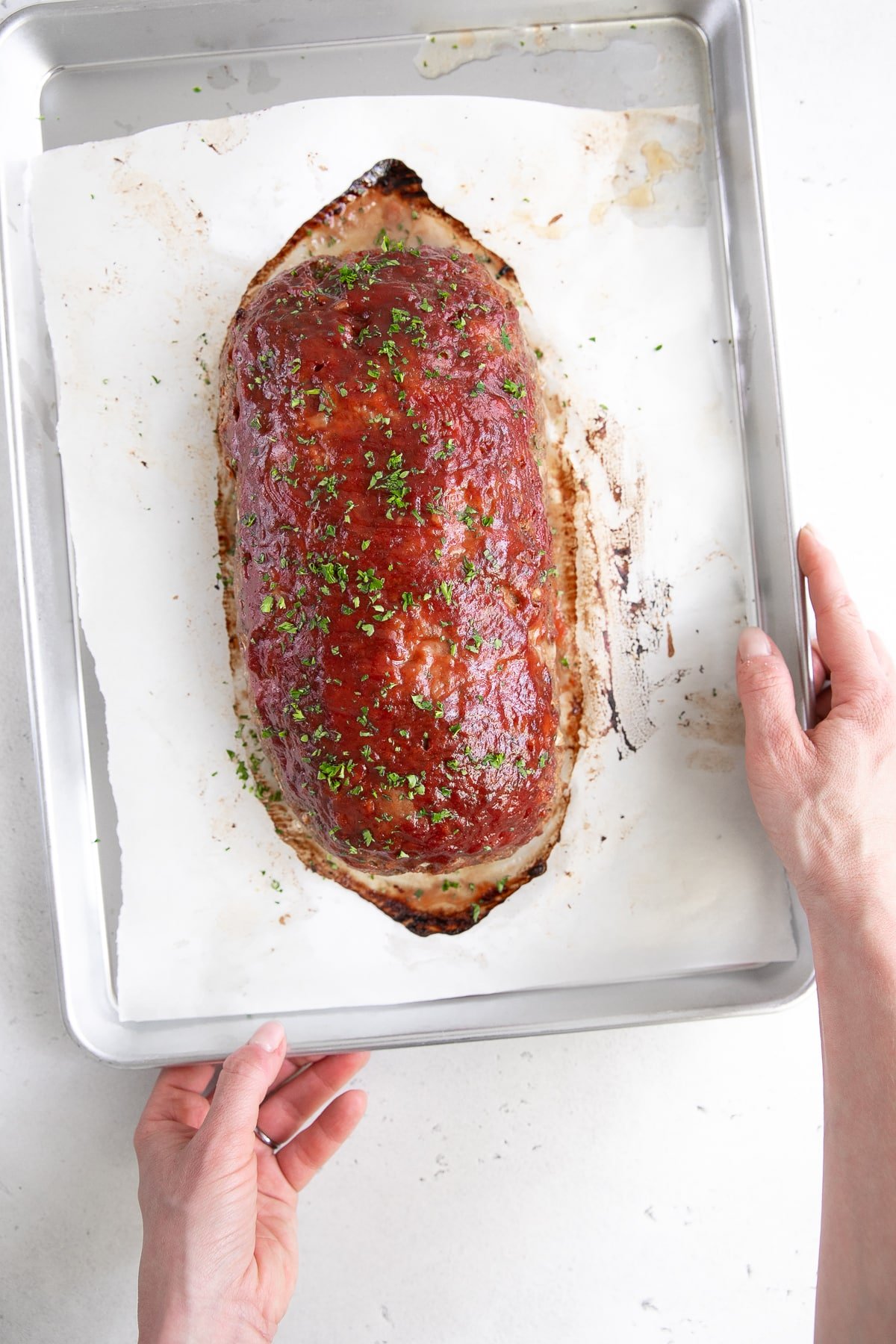Hands holding a baking sheet with the best meatloaf. recipe.