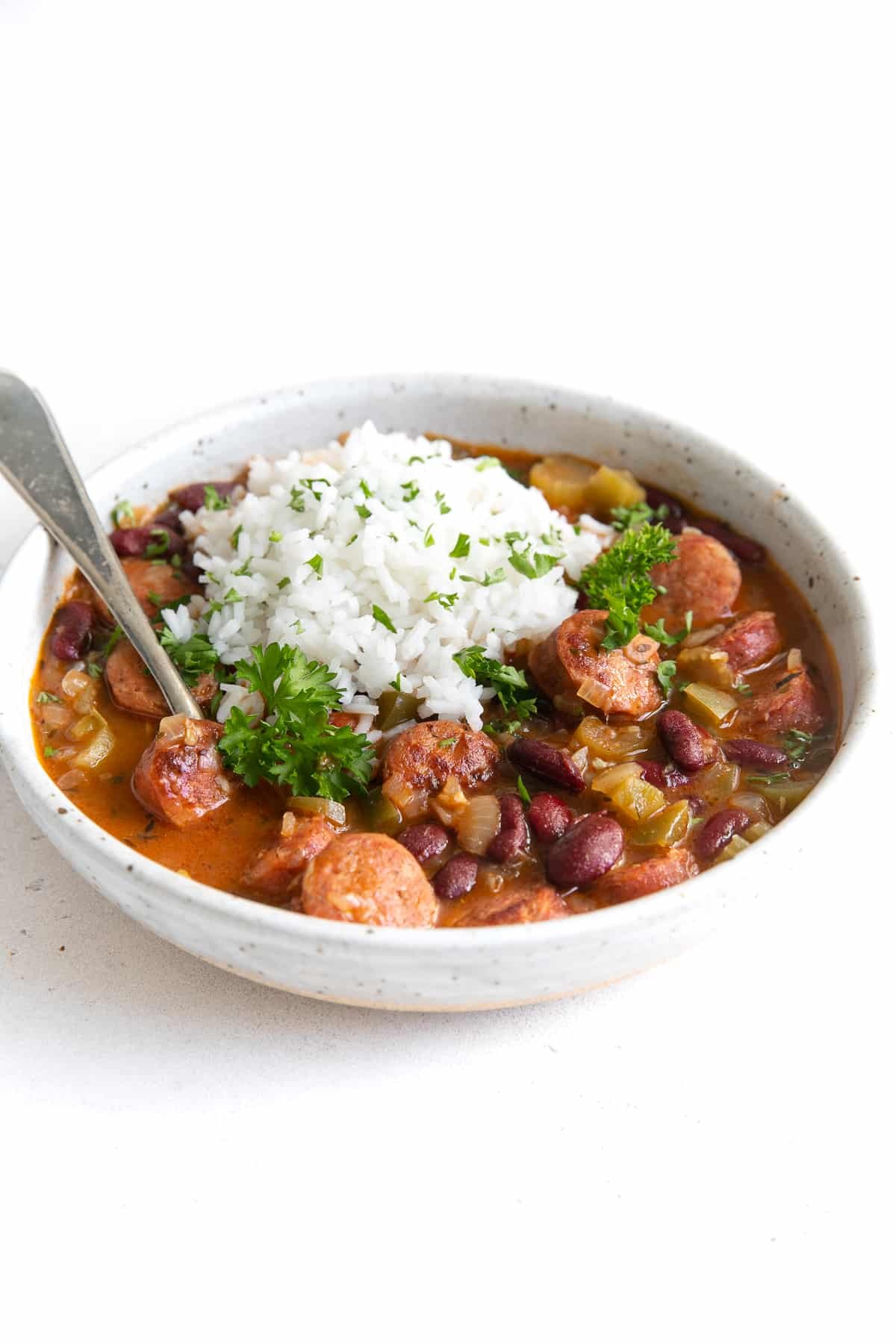 White shallow bowl filled with cooked red beans, andouille sausage, and topped with white rice.