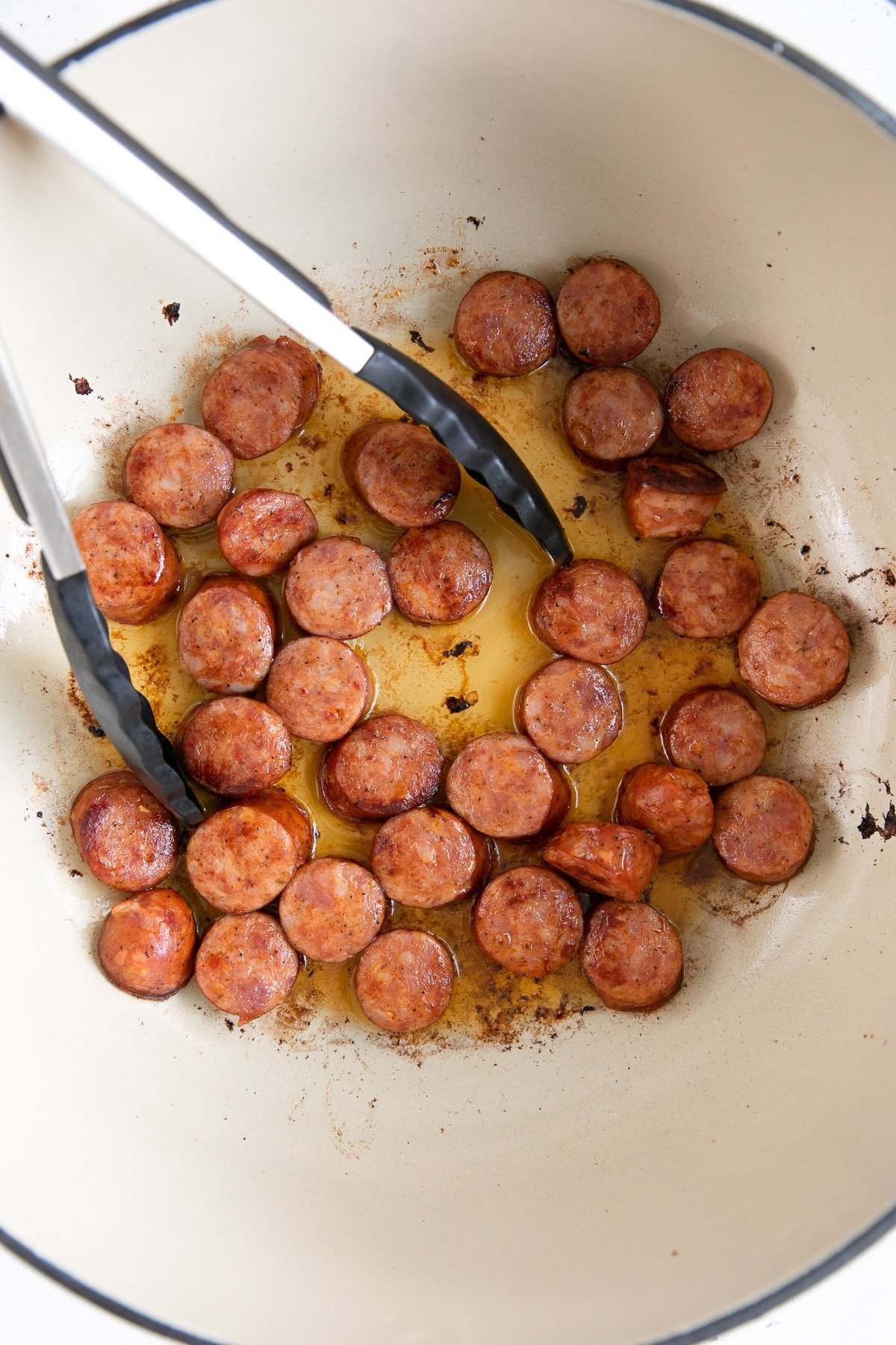 Sliced andouille sausage cooking in a large Dutch oven.