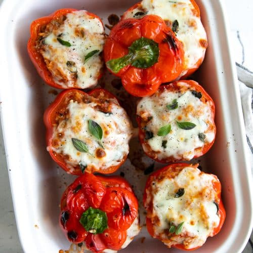 White baking dish filled with red bell peppers stuffed with rice and spaghetti sauce and baked.