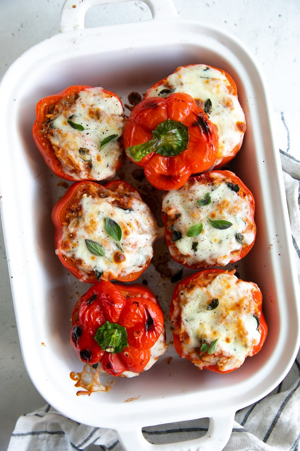 White baking dish filled with red bell peppers stuffed with rice and spaghetti sauce and baked.