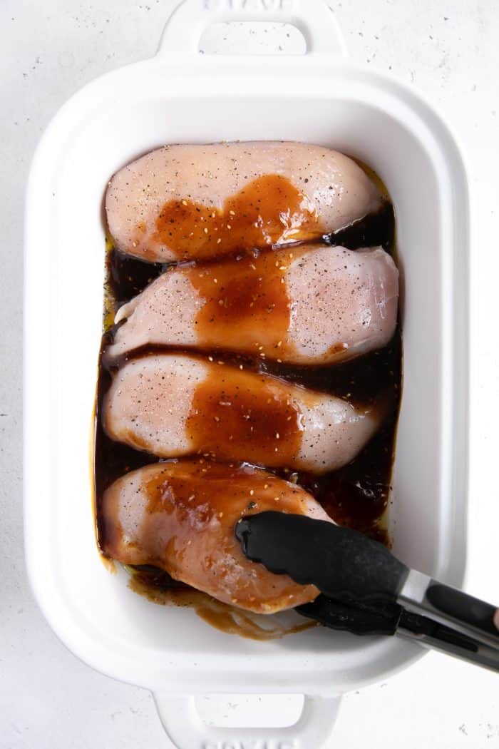 Four raw chicken breasts coated in teriyaki sauce.