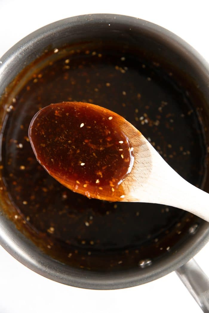 Wooden spoon with thickened teriyaki sauce hovering over saucepan.
