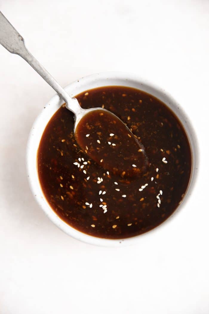 Spoon hovering in a small white bowl with teriyaki sauce.