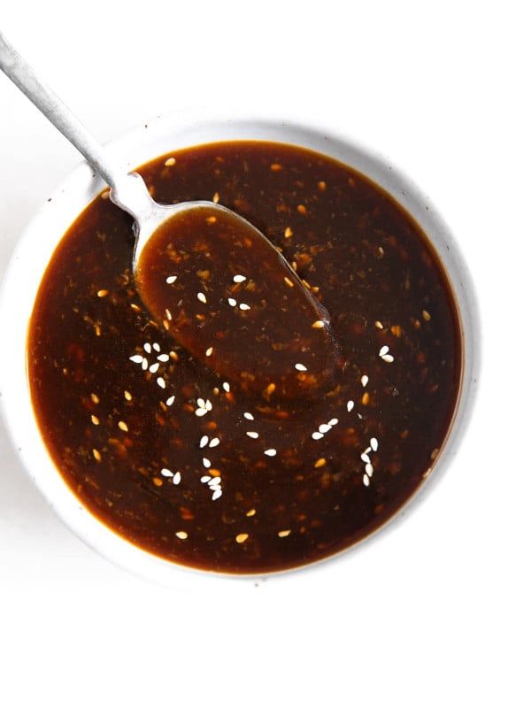 Spoon hovering in a small white bowl with teriyaki sauce.