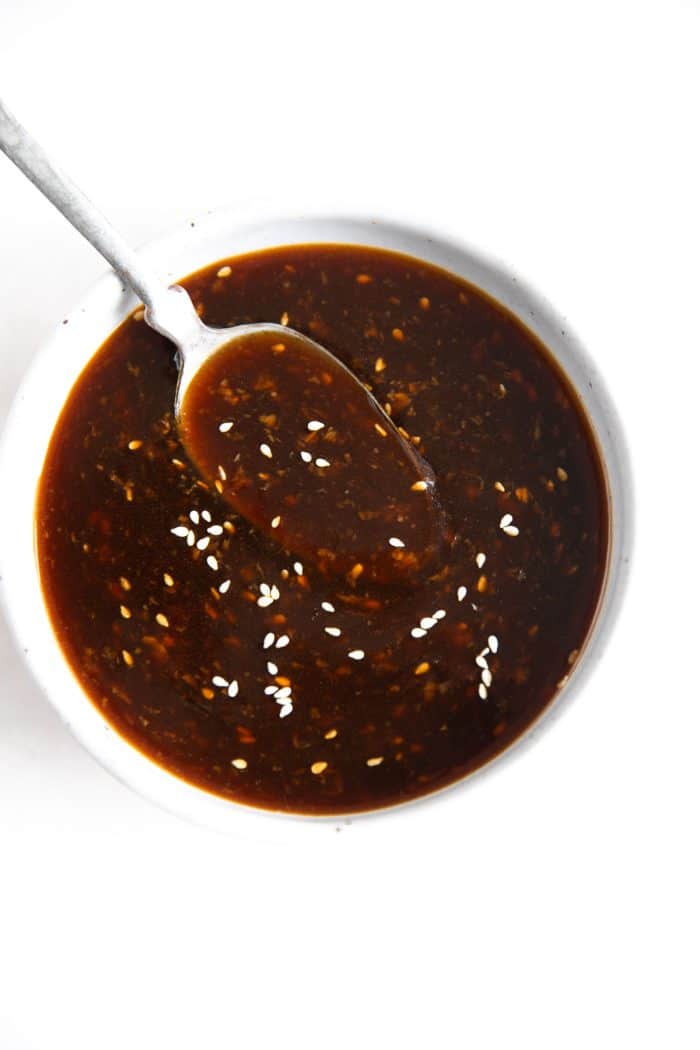 Spoon hovering in a small white bowl with teriyaki sauce.
