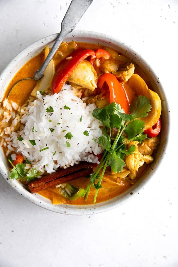 Colorful chicken curry in a large bowl and topped with white rice and fresh cilantro.