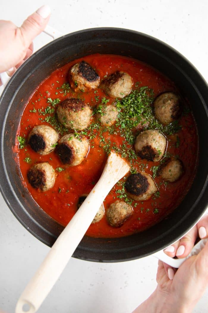 Meatballs added to a large pot of homemade tomato sauce.