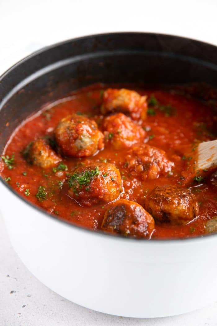 White stock pot filled with meatballs simmering in a homemade tomato sauce.