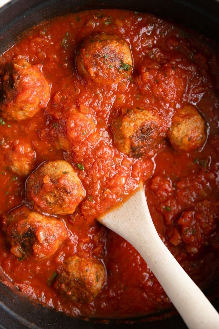 Close up image of meatballs simmering in tomato sauce.