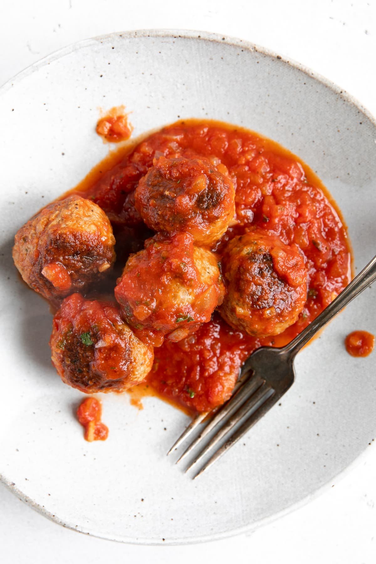 Small white serving plate filled with six homemade beef meatballs covered in tomato sauce.