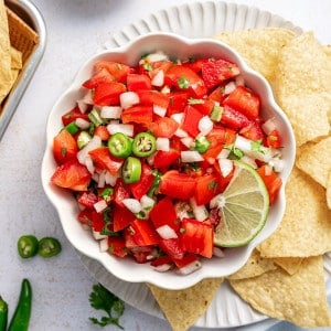 Square overhead shot of pico de gallo in a scalloped white bowl with chips and lime slices.