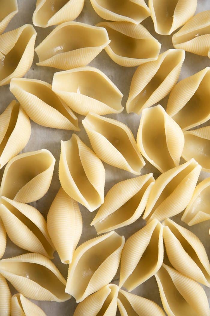 Al dente pasta shells on a large baking sheet lined with parchment paper.
