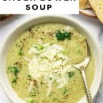 Vertical Pinterest pin featuring a close-up overhead photo of broccoli cauliflower soup in a beige bowl. The soup is creamy pale green with small broccoli bits, topped with shredded cheddar and cracked black pepper, and a gold-handled spoon resting in the bowl. Toasted bread slices appear at the top right, and a black-and-white striped towel is visible at the bottom right. A white text box across the top includes black text โVEGETARIAN + GLUTEN FREEโ and large bold title text โBROCCOLI CAULIFLOWER SOUP.โ Small site text โtheforkedspoon.comโ appears near the bottom.