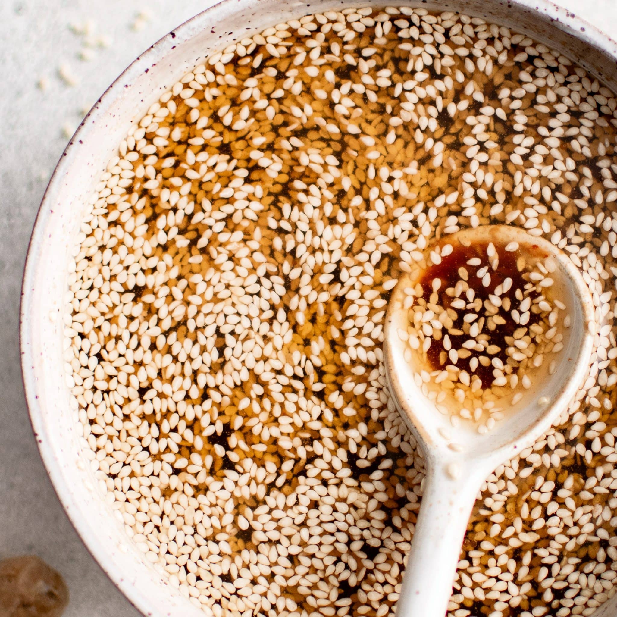 A close-up view of the finished sesame dressing with a ceramic spoon lifting the mixture, showcasing floating sesame seeds and a balanced oil-vinegar emulsion.