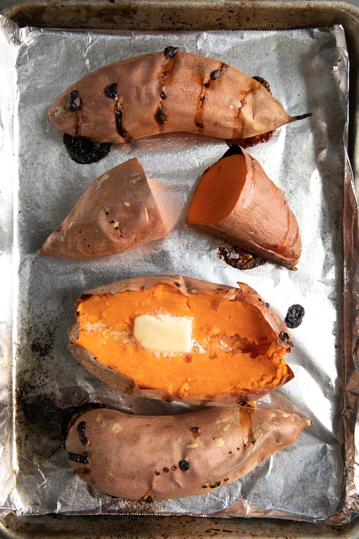 Four fully cooked sweet potatoes on a baking sheet lined with foil.