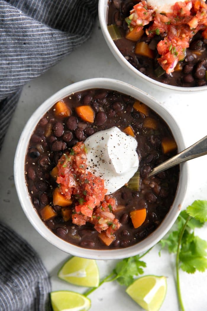 Two white bowls filled with black bean soup and garnished with sour cream and fresh salsa.