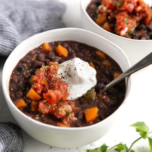 Two white bowls filled with black bean soup and garnished with fresh salsa and sour cream.