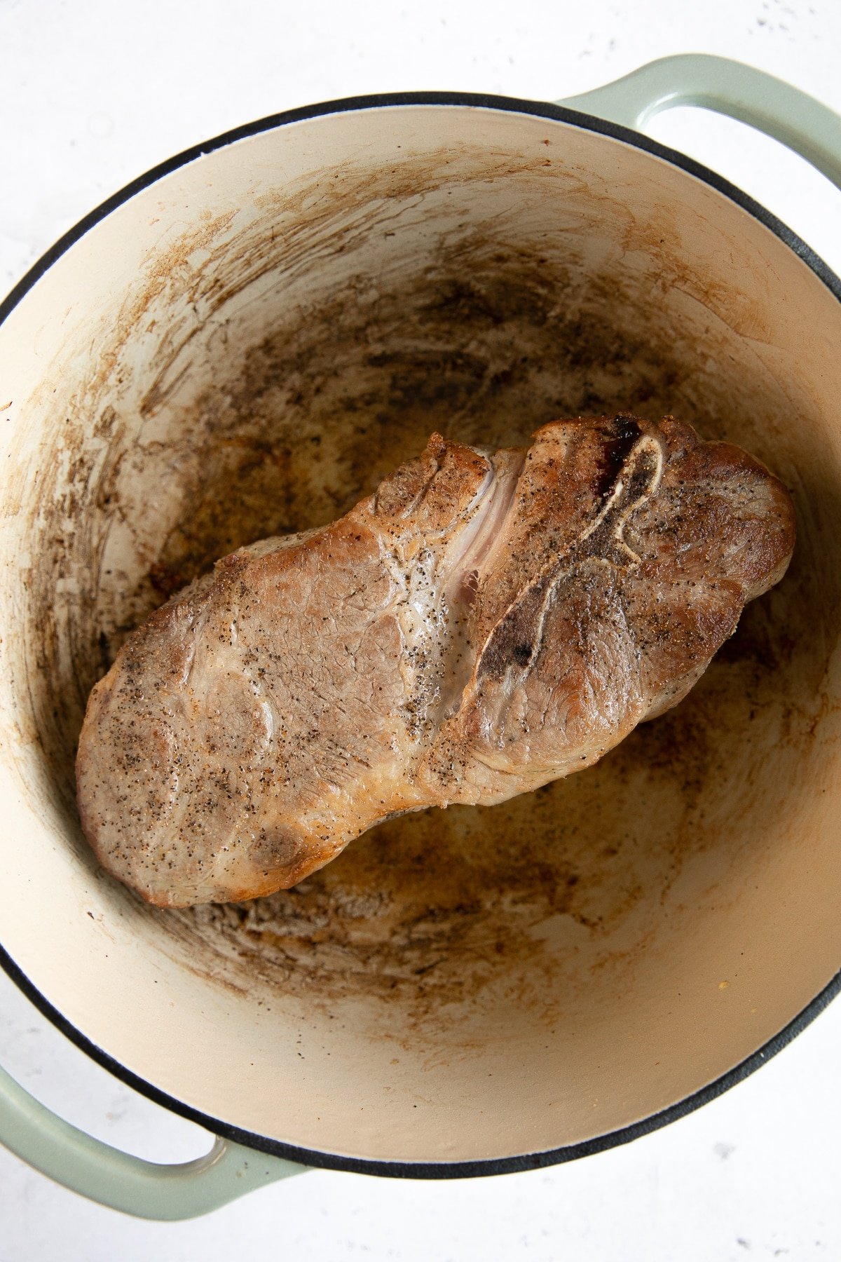 Large bone-in pork shoulder butt roast browning in a large Dutch oven.
