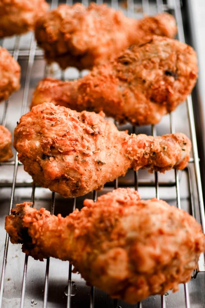 Crispy, golden buttermilk fried chicken drumsticks are cooling on a wire rack on a baking sheet.