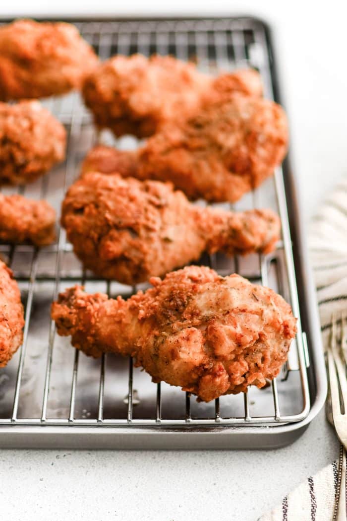 Crispy, golden buttermilk fried chicken drumsticks are cooling on a wire rack on a baking sheet.