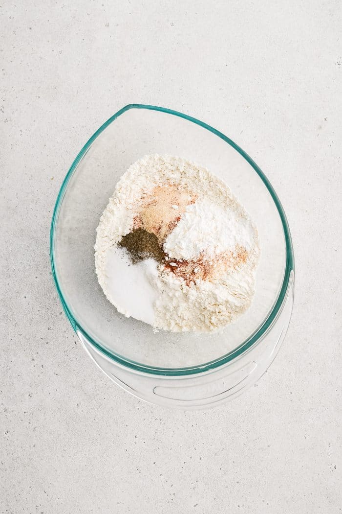 Large glass mixing bowl filled with flour, cornstarch, garlic powder, onion powder, and paprika.