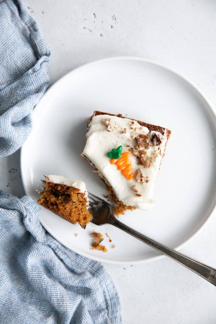 Slice of frosted carrot cake on a white plate.