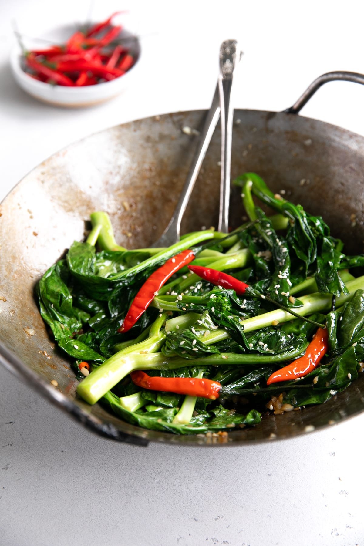 Large wok filled with Chinese broccoli, garlic, and Thai chilis.