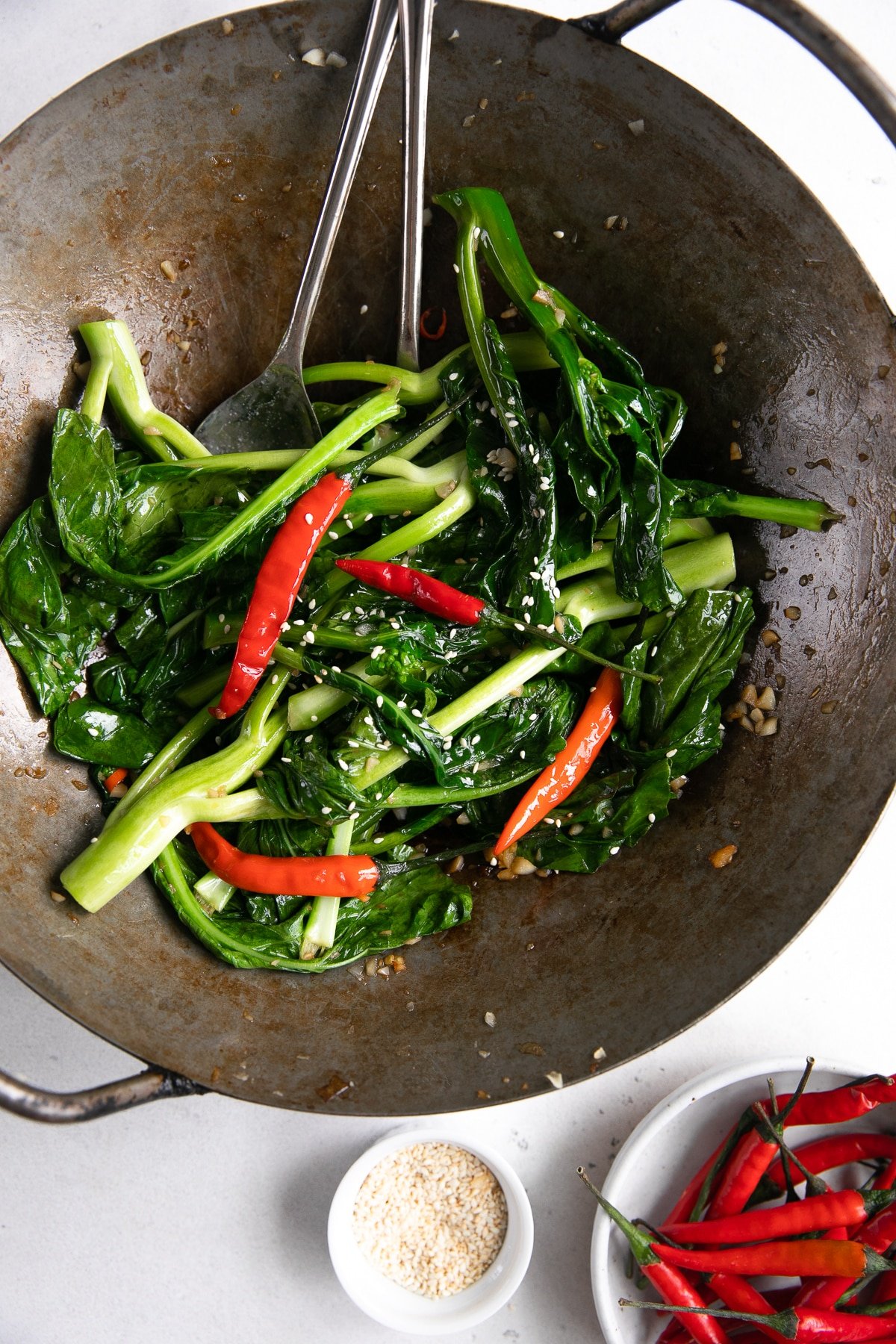 Large wok filled with stir fried Chinese broccoli in garlic and soy sauce with dried Thai chilis.