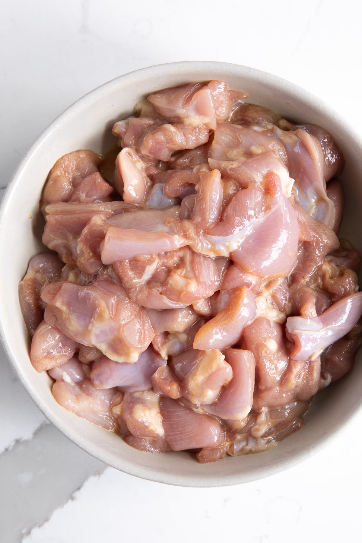 Chicken pieces marinating in a large white bowl.