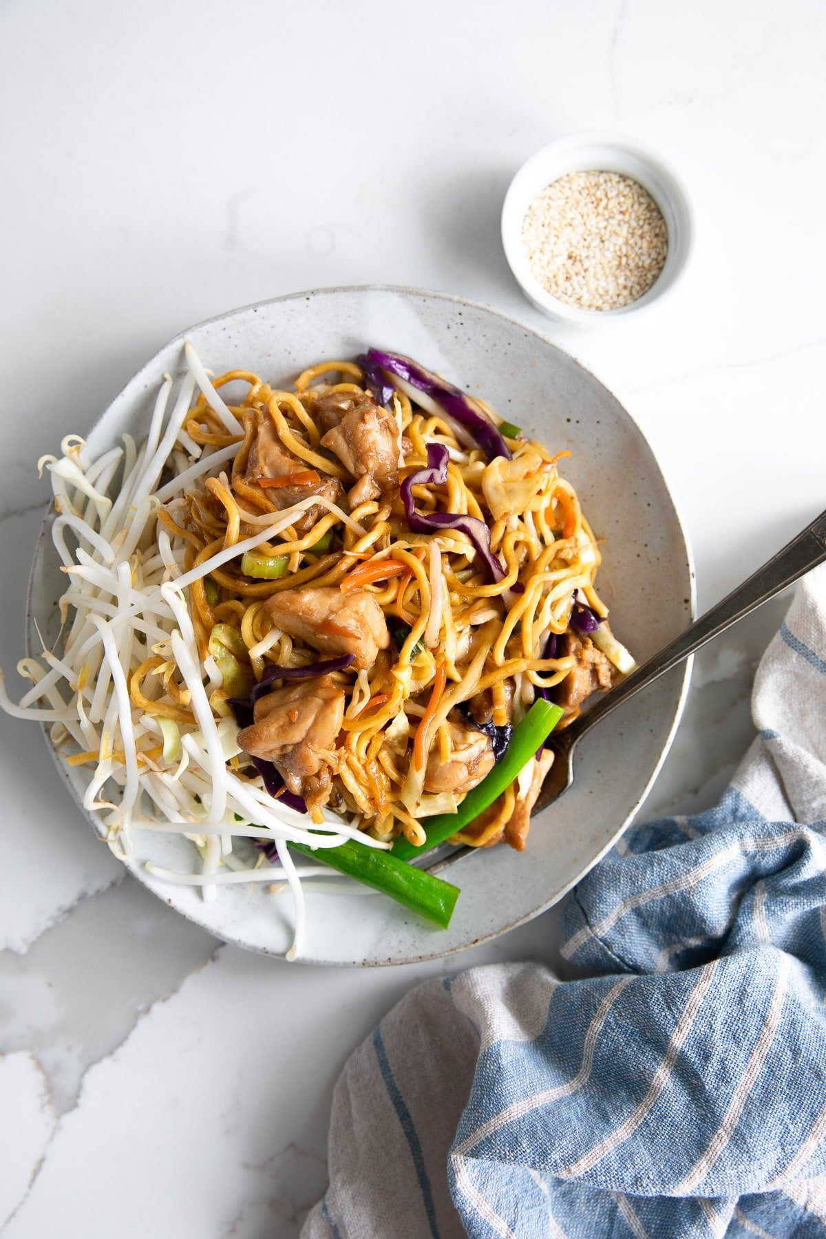 White plate filled with golden chow mein noodles with chicken and vegetables.